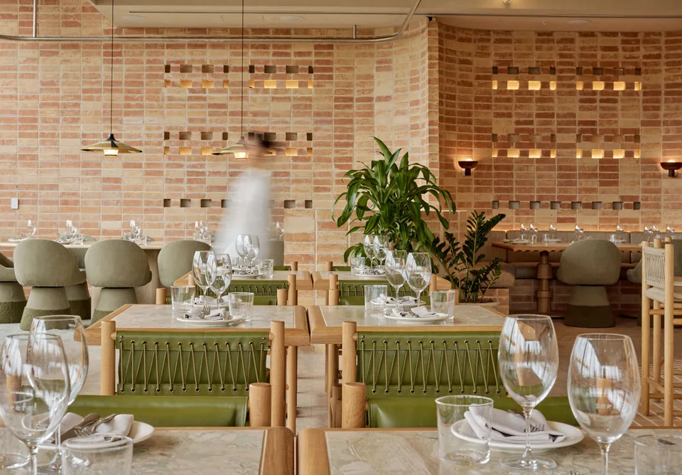 Sunlit dining room at Hamsi Taverna with green chairs, timber furniture and brickwork.