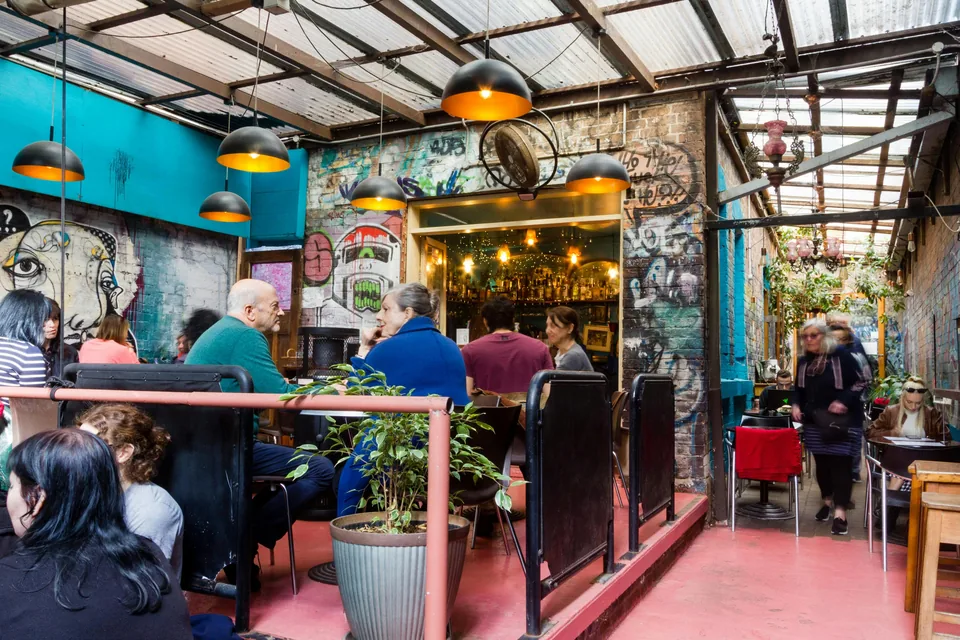 Customers in Sappho’s covered courtyard beside the bar, colourful graffiti and hanging lamps.