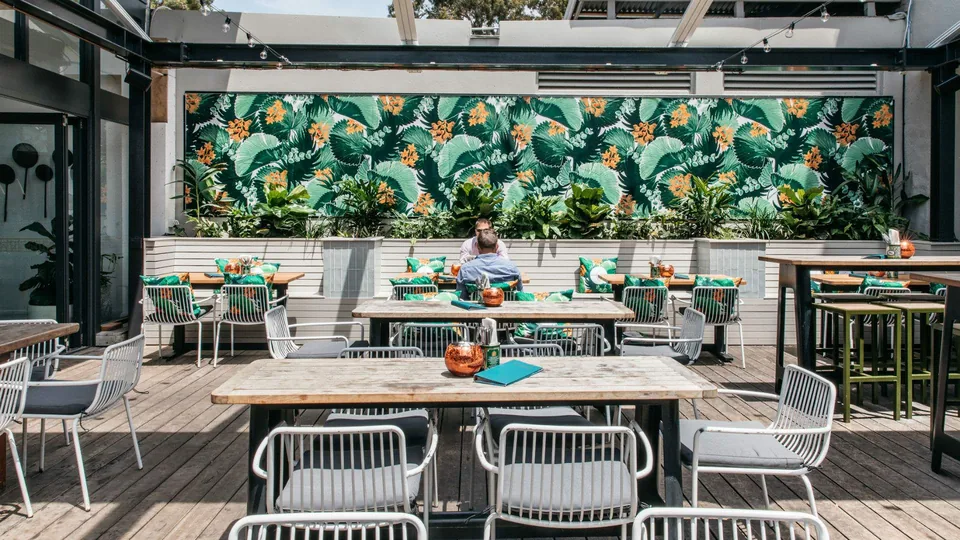 Sunny courtyard at The Toxteth with timber tables, green cushions and a tropical mural.